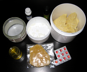 Ingredients for creams: small vials on top are essential oils; jars from the left are coconut oil, shea butter, and cacao butter; bottom has a jar of jojoba oil, beeswax piece, and capsules of vitamin E.
