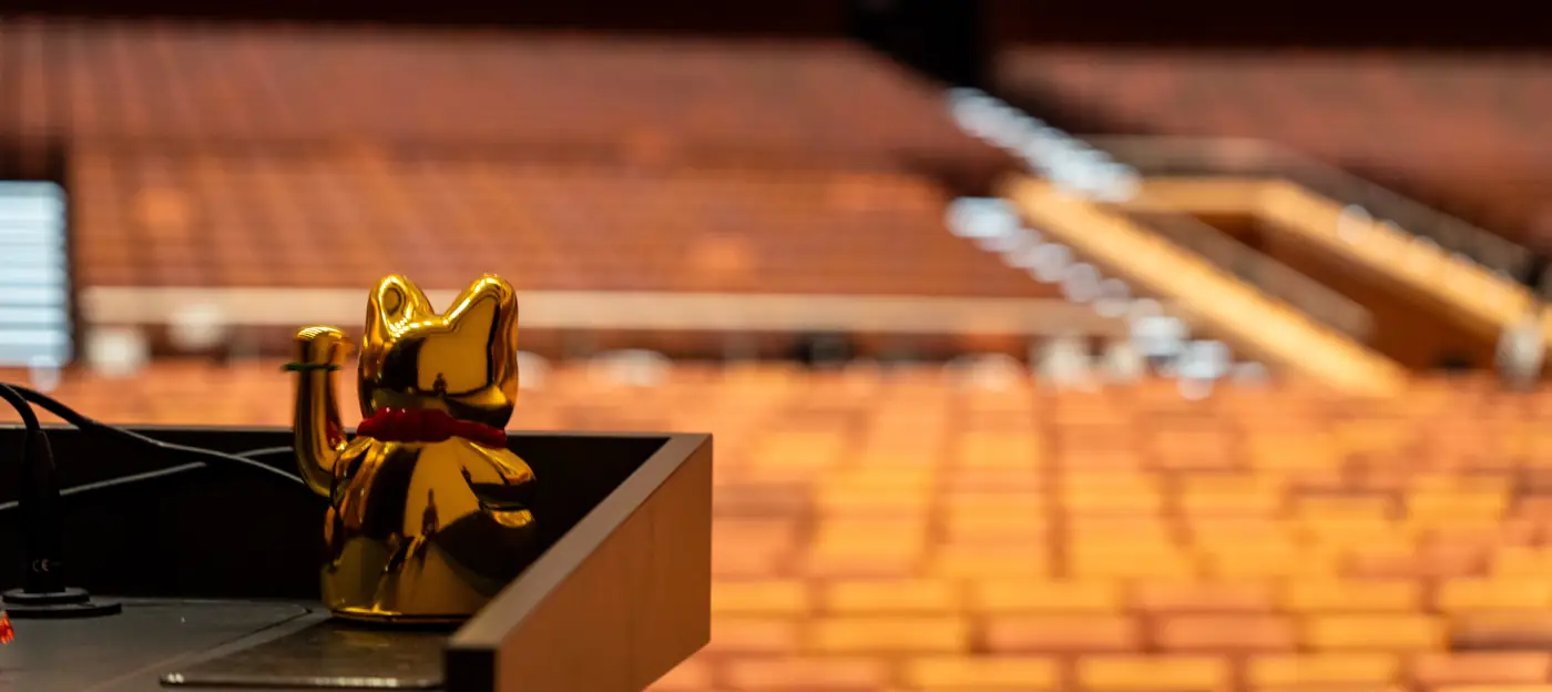 View from the stage into an empty hall 1. A winkekatze sits on the desk.