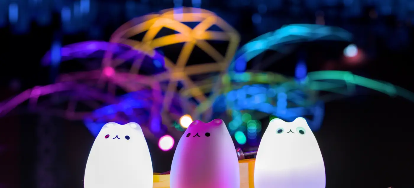 3 farbig beleuchtete Blinkekatzen, im Hintergrund eine beleuchtete Palmenkonstruktion