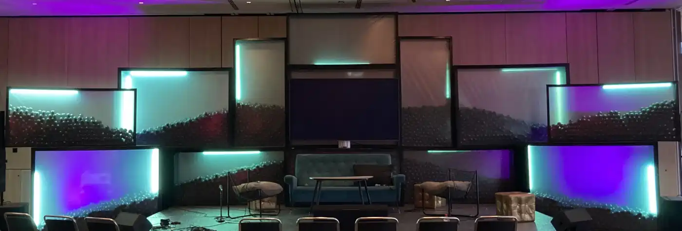 Eine Bühne mit geheimnisvollen Objekten in beleuchteten Glaskästen. Auf der Bühne stehen ein Sofa, ein Tisch, zwei Sessel und drei Sitzwürfel.