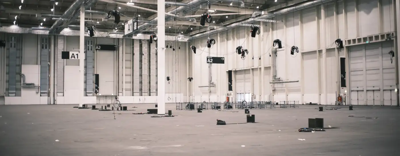 Bild der leeren Messehalle A1 der Messe Hamburg. es hängen Scheinwerfer von der Decke und Auf dem Bodenliegen Kabel und Bühnentechnik